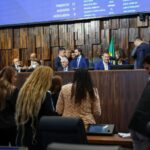 Plenário da Assembleia Legislativa do Estado do Rio de Janeiro durante sessão extraordinária. Parlamentares e assessores ocupam o plenário enquanto a Mesa Diretora conduz os trabalhos. Ao fundo, o painel eletrônico exibe o quórum da sessão e a presença dos deputados.