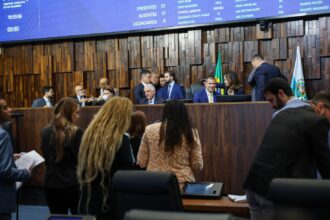 Plenário da Assembleia Legislativa do Estado do Rio de Janeiro durante sessão extraordinária. Parlamentares e assessores ocupam o plenário enquanto a Mesa Diretora conduz os trabalhos. Ao fundo, o painel eletrônico exibe o quórum da sessão e a presença dos deputados.