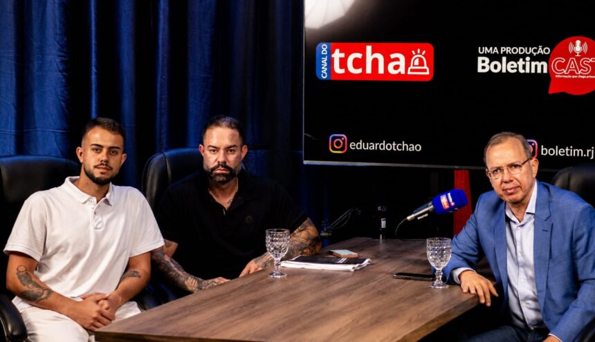 Poubel e o filho, pré-candidato à Alerj, posam ao lado do jornalista Eduardo Tchao durante a gravação do Boletim Cast, em estúdio com mesa, microfones e painel do programa ao fundo.