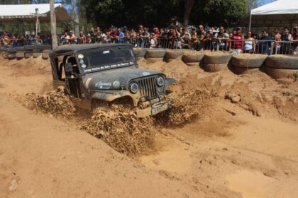 Jipe atravessa uma pista de lama durante o Encontro Nacional de Jipeiros em Atafona, acompanhado pelo público.
