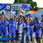Jogadores e integrantes do Goytacaz comemoram o título da Série B2 do Campeonato Carioca com o troféu erguido.