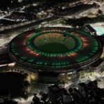 Vista aérea noturna do Maracanã iluminado nas cores verde e vermelha, no Rio de Janeiro.