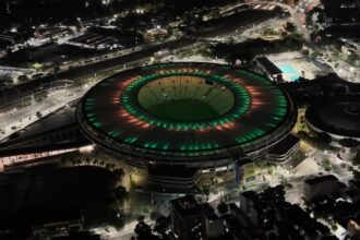 Vista aérea noturna do Maracanã iluminado nas cores verde e vermelha, no Rio de Janeiro.