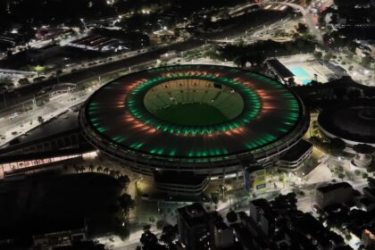 Vista aérea noturna do Maracanã iluminado nas cores verde e vermelha, no Rio de Janeiro.