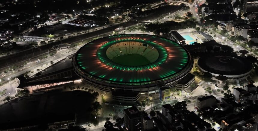 Vista aérea noturna do Maracanã iluminado nas cores verde e vermelha, no Rio de Janeiro.