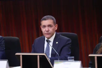 Presidente do TSE, ministro Kassio Nunes Marques, sentado diante de um microfone durante cerimônia do tribunal.