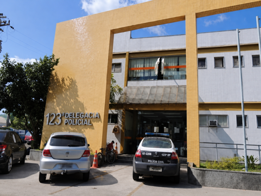 Fachada da 123ª Delegacia de Polícia de Macaé, com carros e uma viatura estacionados em frente ao prédio.