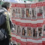 Homem observa um painel coberto por cartazes com fotografias e informações sobre pessoas desaparecidas.