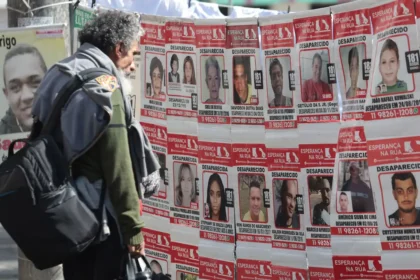 Homem observa um painel coberto por cartazes com fotografias e informações sobre pessoas desaparecidas.