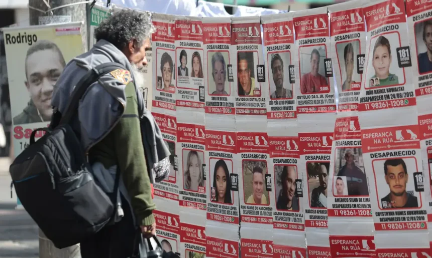 Homem observa um painel coberto por cartazes com fotografias e informações sobre pessoas desaparecidas.
