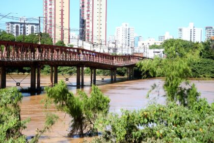Ponte Barcelos Martins atravessa o Rio Paraíba do Sul, com vegetação nas margens e prédios de Campos ao fundo.