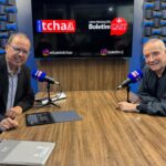 O jornalista Eduardo Tchao entrevista o empresário Eike Batista no estúdio do Boletim Cast. Os dois estão sentados frente a frente, diante de uma mesa com microfones, enquanto ao fundo um monitor exibe as marcas do Canal do Tchao e do Boletim Cast.