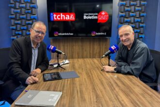O jornalista Eduardo Tchao entrevista o empresário Eike Batista no estúdio do Boletim Cast. Os dois estão sentados frente a frente, diante de uma mesa com microfones, enquanto ao fundo um monitor exibe as marcas do Canal do Tchao e do Boletim Cast.