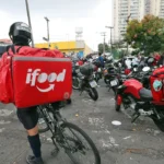 Entregador do iFood com bicicleta em meio a motocicletas e outros trabalhadores de aplicativos.