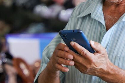 Homem segura e utiliza um telefone celular em um local público.