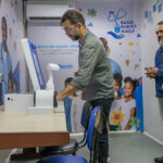 Profissional demonstra equipamentos de Telessaúde em sala de atendimento pediátrico da UPA da Barra, em Macaé, enquanto outras duas pessoas observam.
